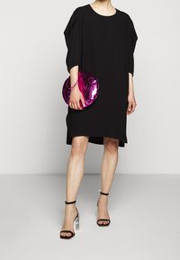 Svart överdimensionerad klänning med korta, lösa ärmar; kombinerad med en rund, metallisk rosa clutch och svartvita randiga klacksandaler.