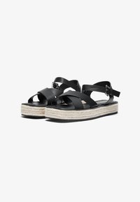 Sorte svart skinnsandaler med kryssende stropper, med en espadrille-stil hempe midtsåle og en lav, flat såle med spenne lukking.