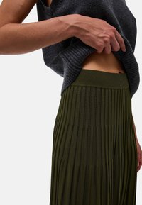 Jupe plissée vert olive avec une taille côtelée, associée à un haut sans manches gris foncé mettant en avant un matériau tricoté texturé.