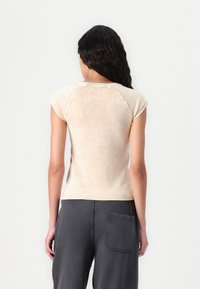Short-sleeve, fitted top in light beige fabric with a soft, textured finish; features raglan sleeves and a round neckline.