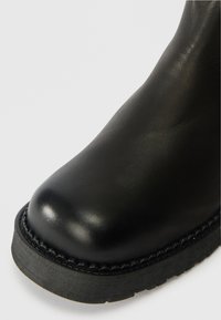 Schwarze Lederstiefel mit runder Spitze, strukturiertem Obermaterial und robuster schwarzer Sohle. Verfügt über eine dekorative Naht entlang der Sohlenkante.