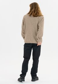 Beige texturerad tröja med långa ärmar, kombinerad med svarta, flerpanelade cargobyxor. Modellen vänder sig bort, skor i svart.