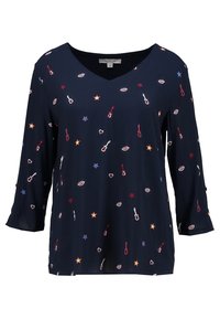 Blouse marine à col en V, ornée d'un motif d'instruments de musique, d'étoiles et de lèvres en rouge, blanc et bleu. Manches trois-quarts.