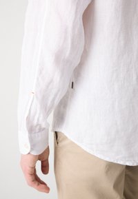 Witte linnen shirt met een zichtbare knoopmanchet en een gebogen zoom. De stof is lichtgewicht met een licht gestructureerde afwerking.