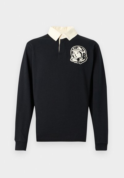 Μαύρο πόλο πουκάμισο με μακριά μανίκια, με γιακά σε κρεμ χρώμα και σχέδιο αστροναύτη στο αριστερό στήθος. Κατασκευασμένο από βαμβακερό ύφασμα.