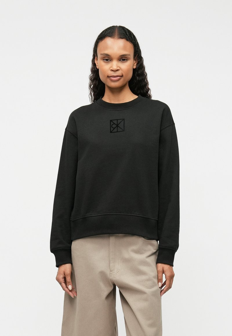 Μαύρο φούτερ με στρογγυλή λαιμόκοψη, φουσκωτά μανίκια και μικρό ανάγλυφο λογότυπο στο στήθος. Κατασκευασμένο από μαλακό, υφασμάτινο υλικό.