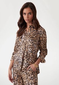 Chemise à motifs léopard en tissu léger, avec deux poches poitrine, manches repliées et coupe décontractée. Boutons dorés en accent.