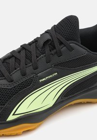 Chaussure de sport noire avec tige en mesh, accents vert lime et design texturé. Dispose d'une semelle marron clair et de lacets noirs.