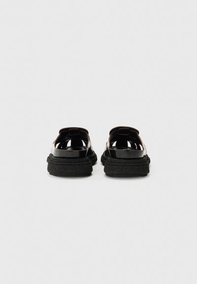 Pantofi negri din piele lacuită, tip slip-on, cu o talpă groasă neagră texturată, având un vârf rotunjit și fără accesorii sau detalii vizibile.