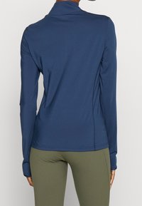 Marinblå långärmad skjorta i mjukt, elastiskt tyg med figursydd design, platta sömmar och en subtil krage, kombinerad med olivgröna leggings.