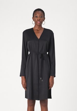 Black, long-sleeve dress with a V-neck and a cinched waist tied with a belt. Smooth texture and a straight cut, reaching mid-thigh.