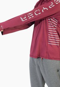 Bordowa sportowa koszulka z długim rękawem z białymi grafikami, z bocznym panelem w paski, w połączeniu z szarymi, teksturowanymi spodenkami dresowymi.