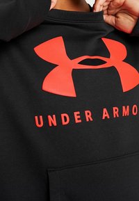 Felpa nera in misto cotone. Presenta un grande logo rosso Under Armour e del testo. Include una tasca frontale e un colletto a coste.