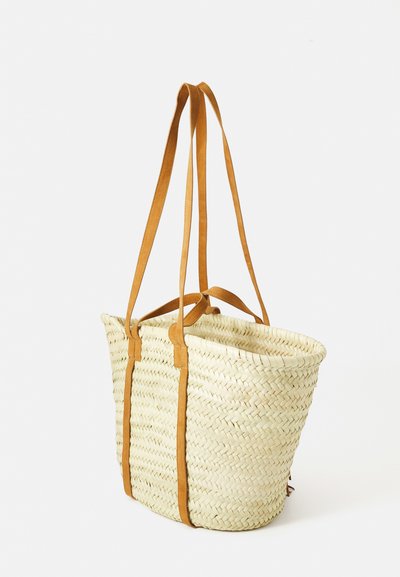 Sac en paille tressée avec deux longues et deux courtes poignées en cuir beige, posé sur fond blanc.