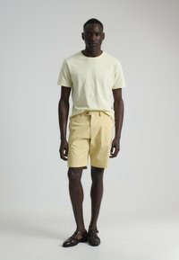 Camiseta de color amarillo claro combinada con pantalones cortos amarillos pálidos. El conjunto tiene un corte relajado, textura de algodón suave y un diseño sencillo. Zapatos marrón oscuro.