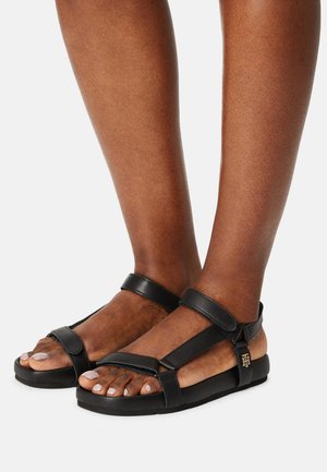 Sorte lædersandaler med to justerbare stropper, et bredt tåområde og en tekstureret sål. Har et lille guld logo-accents på siden.