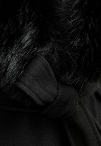 Cappotto nero con un morbido colletto in pelliccia, legato con una cintura in tessuto. Presenta una texture liscia e un design senza cuciture.