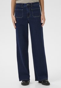 Jeans z szerokimi nogawkami wykonane z ciemnoniebieskiego denimu. Posiadają wysoki stan, kontrastowe szwy, dwie przednie kieszenie oraz zapięcie na guzik.