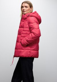 Růžová prošívaná péřová bunda s kapucí, s prošitým vzorem, bočními kapsami a nastavitelným stahováním v pase pro těsné přizpůsobení.