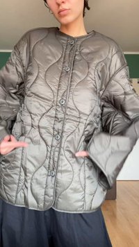 Chaqueta acolchada y gris con un patrón de olas, grandes botones y bolsillos laterales; cuenta con mangas anchas y cuello redondeado.