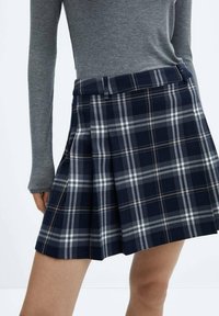 Jupe plissée à carreaux navy avec des motifs blancs et gris, dotée d'une taille ajustée et d'une texture de tissu douce.