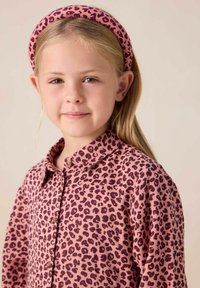 Chemise rose avec un motif léopard, dotée d'un col et d'une fermeture à boutons. Bandeau assorti rose avec un design léopard similaire.