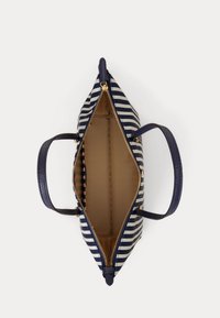 Τσάντα χειρός με ναυτικό μπλε και λευκές ρίγες, με ναυτικό μπλε λαβές και χρυστό φερμουάρ, εμφανιζόμενη ανοιχτή από πάνω, αποκαλύπτοντας εσωτερικό σε απόχρωση ταμπά.