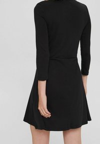 Svart långärmad klänning med en åtsittande bodice och utsvängd kjol. Slät textur med en enkel design och rund krage.