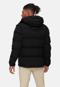 Zwarte pufferjack met een capuchon en elastische manchetten, met geborduurde segmenten. De merknaam "Mammut" staat op de achterkant gedrukt.