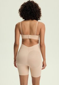 Nude shapewear featuring a low back design, adjustable straps, and a fitted bodice extending to mid-thigh. Smooth texture and seamless finish.