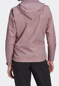 Světlounce růžová nepromokavá bunda s kapucí, hladkým povrchem, nastavitelnými manžetami a jednoduchým designem. Vyznačuje se minimalistickým stylem.