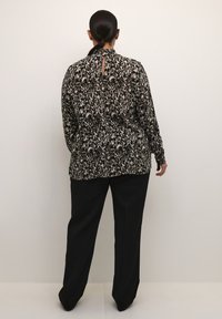 Blusa a maniche lunghe nera e beige con motivo floreale, dotata di dettaglio a chiave sulla schiena, abbinata a pantaloni neri a gamba larga.