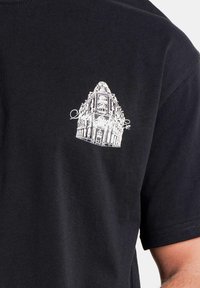 Zwarte katoenen T-shirt met een witte architectonische grafiek op de borst. Korte mouwen en een ronde hals. Gladde textuur.