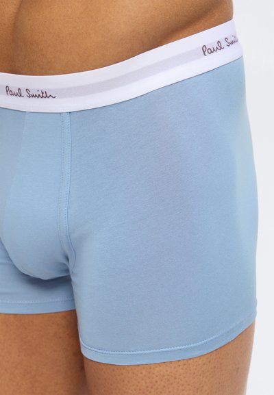 Κοντινό πλάνο ενός ατόμου που φοράει ανοιχτό μπλε σλιπ boxer με λευκή μέση που φέρει την επιγραφή "Paul Smith".