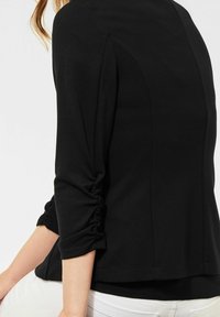 Černý vršek s tříčtvrtečními rukávy, který má nařasené detaily, hladkou texturu a rovný lem.