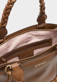 Sac à main en cuir marron avec une poignée tressée, quincaillerie dorée, et un intérieur zippé comportant une doublure imprimée du logo et une poche supplémentaire.