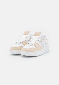 Beige og hvite joggesko med en glatt lær overdel, teksturerte semskede detaljer, perforert tåboks, og hvit gummisåle.