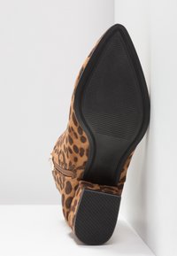 Bottine à bout pointu imprimé léopard avec talon épais, texture visible de la semelle et fermeture éclair latérale sur fond blanc en coin.