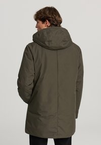 Cappotto imbottito verde oliva scuro con cappuccio, caratterizzato da un design semplice, una texture liscia e un taglio dritto, che termina poco sopra il ginocchio.