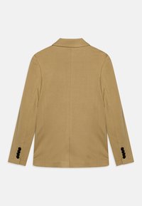 Barna zakó, kihajtható gallérral, egyetlen szellőzőnyílással és fekete gombokkal a mandzsettán. Simább textúrájú és testre szabott dizájn. Hátulnézeti kép.