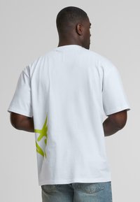White cotton t-shirt with short sleeves, featuring a large green graphic design on the left side. The fabric appears smooth and breathable.