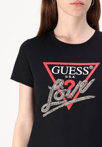 Melnās krāsas T-krekls ar sarkano trīsstūra dizainu, baltu zīmola logotipu un uzpūsto "Love" tekstu kursīvā.