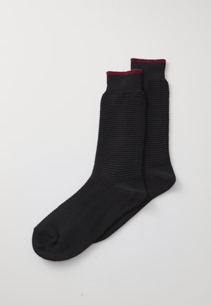 Schwarze Baumwollsocken mit gerippter Textur und bordeauxrotem Besatz am oberen Rand. Entworfen für Komfort und Vielseitigkeit.