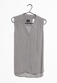 Ärmlös blus i grått tyg med ett geometriskt mönster i orange och kräm. Har en V-halsringning och en rundad fåll. Hänger på en svart krok.