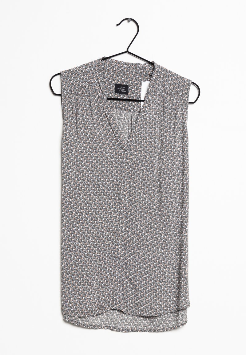 Ärmlös blus i grått tyg med ett geometriskt mönster i orange och kräm. Har en V-halsringning och en rundad fåll. Hänger på en svart krok.