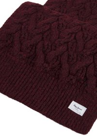Mørk burgunder strikket beanie med kabelmønstre og et lille hvidt stofmærke syet nær kanten.