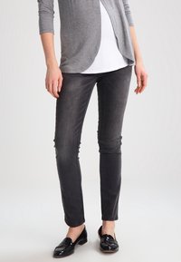 Cardigan gris de manga larga sobre una blusa blanca, combinado con jeans negros ajustados y mocasines negros brillantes. Tejido suave y diseño ajustado.
