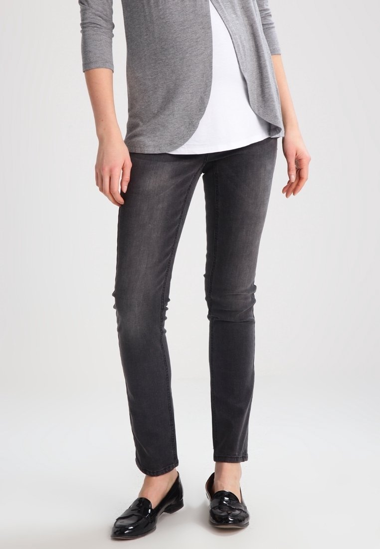 Cardigan gris de manga larga sobre una blusa blanca, combinado con jeans negros ajustados y mocasines negros brillantes. Tejido suave y diseño ajustado.
