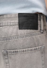 Ανοιχτό γκρι τζιν τζιν με μαύρο δερμάτινο πατς με την επιγραφή "JACK & JONES", φορεμένα με πουκάμισο ανοιχτού γαλάζιου χρώματος που είναι μέσα στη βράκα.