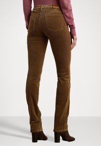 Hnědé manšestrové kalhoty, úzký střih, s hladkou texturou. Dva zadní kapsy, poutko na opasek a nošeny s tmavými botami na podpatku.